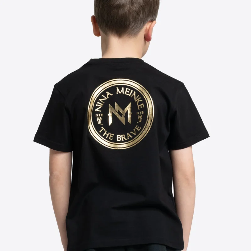 Schwarzes Kinder T-Shirt von BENLEE mit gro&szlig;em rundem R&uuml;ckenprint in Gold, darunter der Schriftzug &bdquo;NINA MEINKE&ldquo; und &bdquo;THE BRAVE&ldquo;.