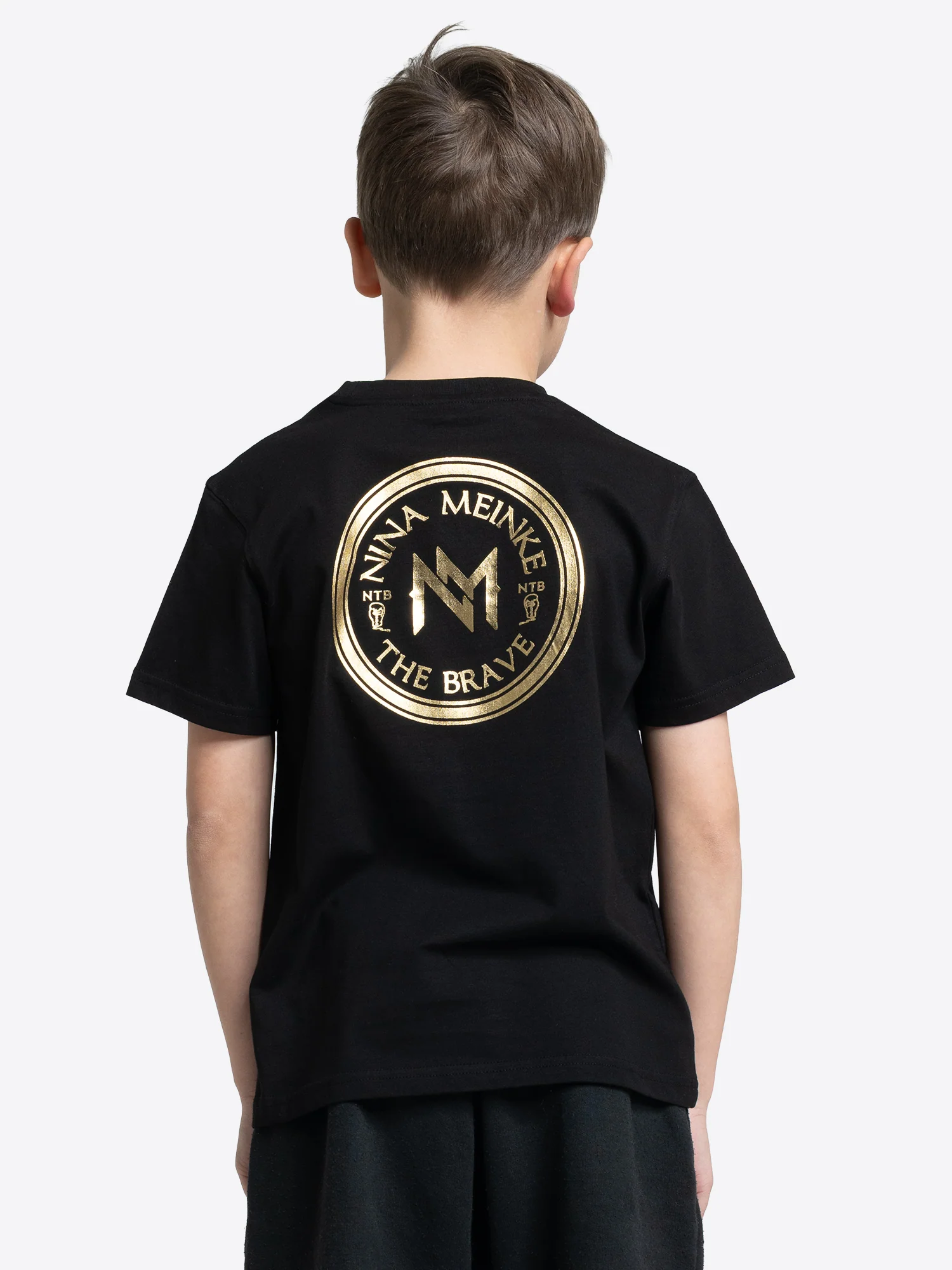 Schwarzes Kinder T-Shirt von BENLEE mit großem rundem Rückenprint in Gold, darunter der Schriftzug „NINA MEINKE“ und „THE BRAVE“.