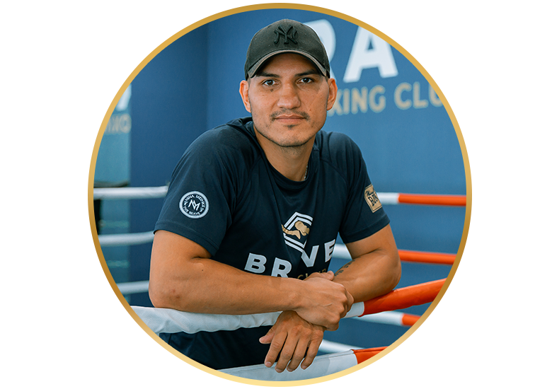 Ein Boxtrainer lehnt mit verschränkten Armen auf den Seilen eines Boxrings im Brave Boxing Club.