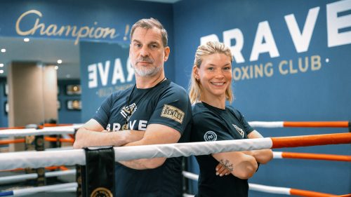 Zwei Trainer im BRAVE Boxing Club stehen im Ring Rücken an Rücken vor der blauen Wand mit Champion-Schriftzug.