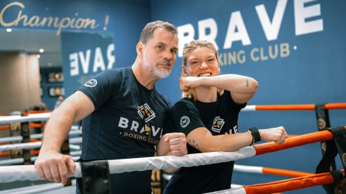 Zwei Mitglieder des Brave Boxing Club posieren lächelnd im Boxring vor einer blauen Wand mit dem Schriftzug Brave.