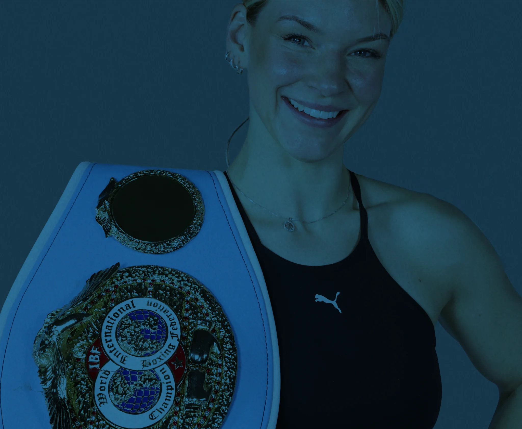 Nina Meinke lächelt und hält einen Boxgürtel in der Hand, während sie in einem schwarzen Sportoberteil posiert.